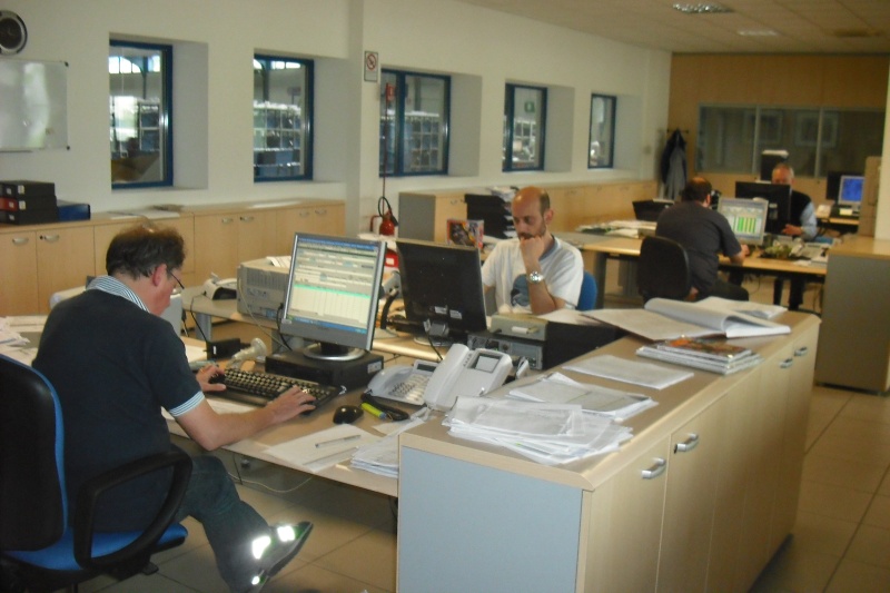 Ufficio diffusione con quattro impiegati ai computer fra telefoni e documenti