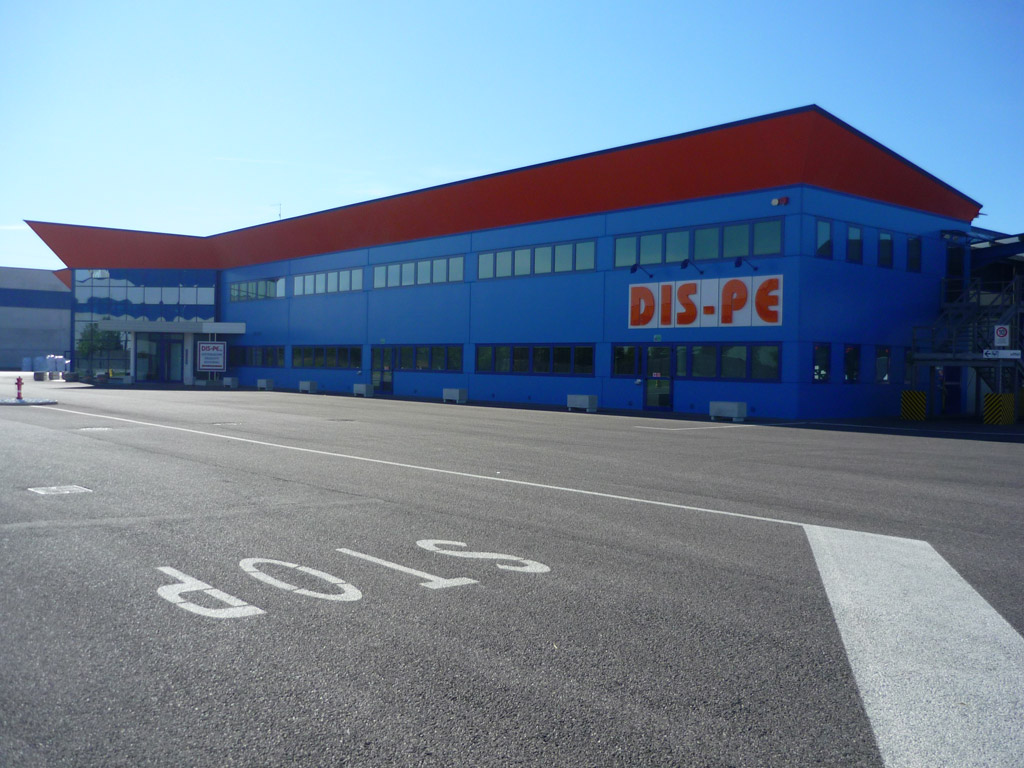 Sede di Udine: magazzino blu con tetto rosso e insegna DIS-PE, piazzale in primo piano